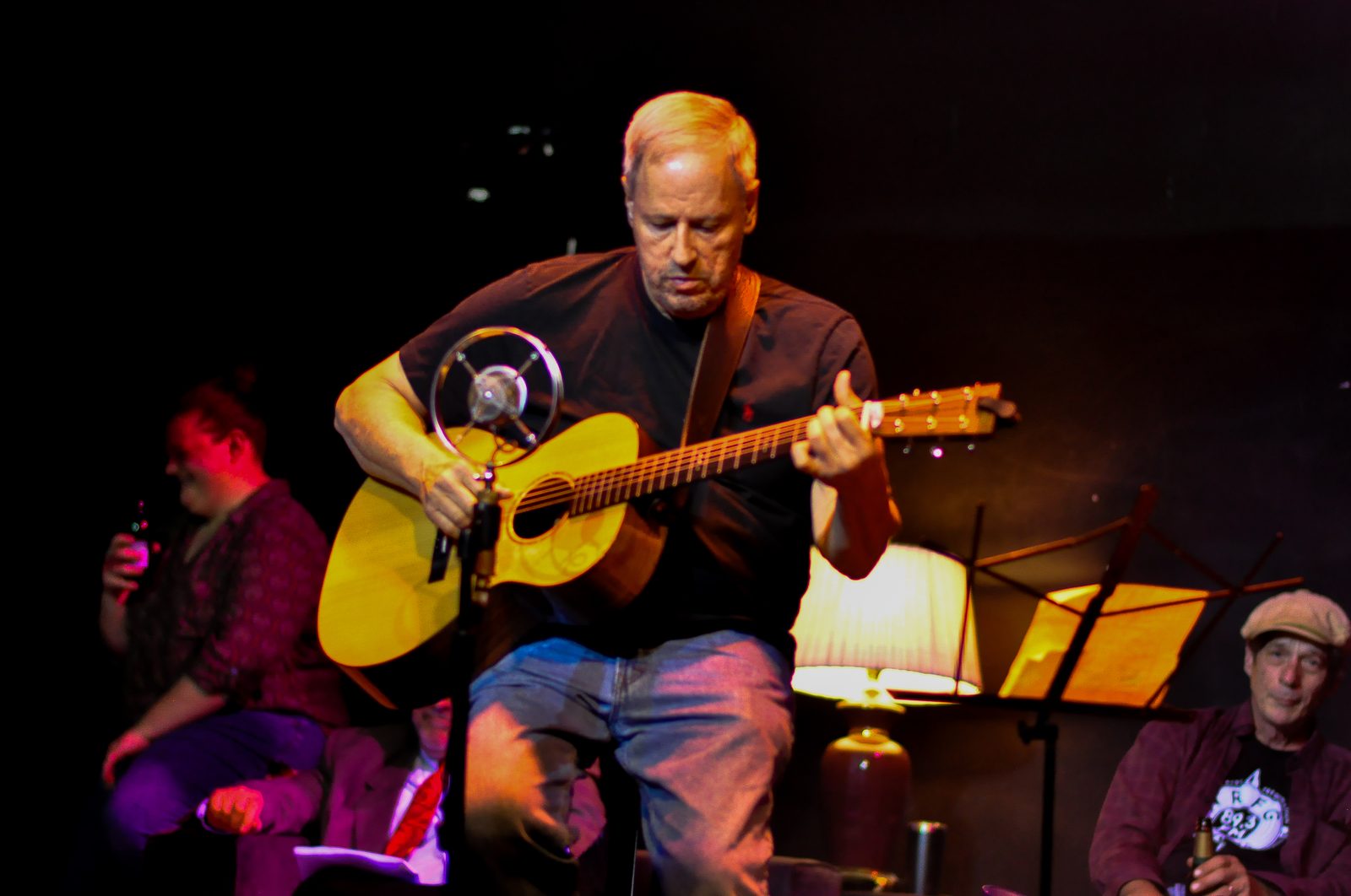Joe Caporaso playing acoustic guitar on a low-lit stage
