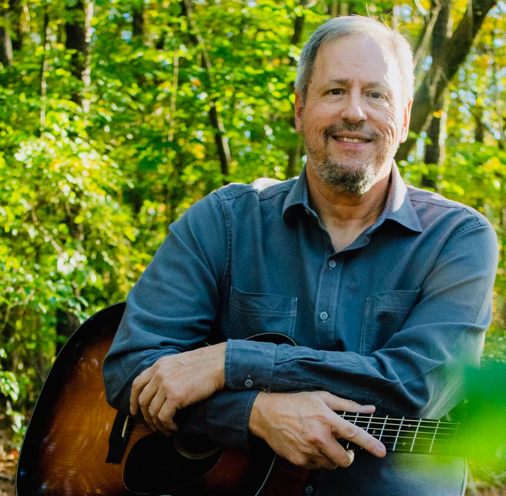 Joe Caporaso holding his acoustic guitar outdoors